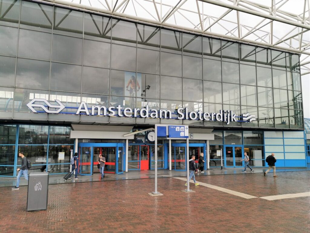 Amsterdam Sloterdijk station features a modern glass facade, bustling travelers, and clear signage.