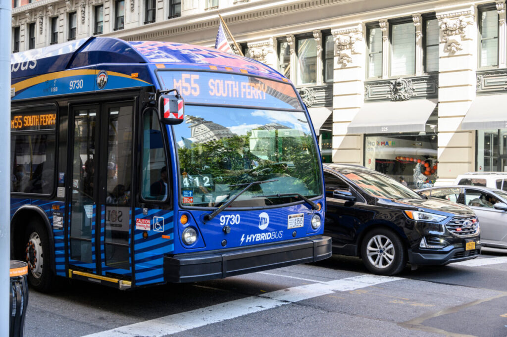 Blue MTA hybrid bus on M55 route, showcasing New York Citys vibrant urban life and architecture.