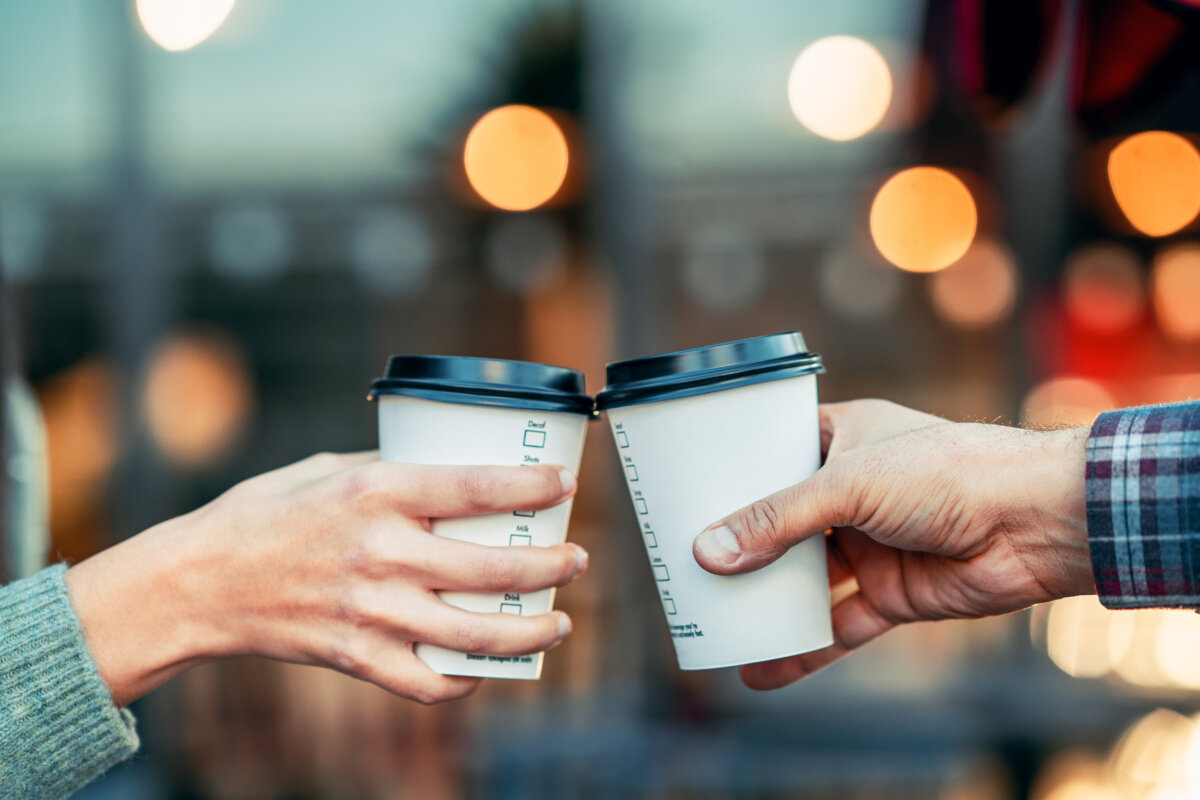 Couple holding coffee cups while waiting to board a bus