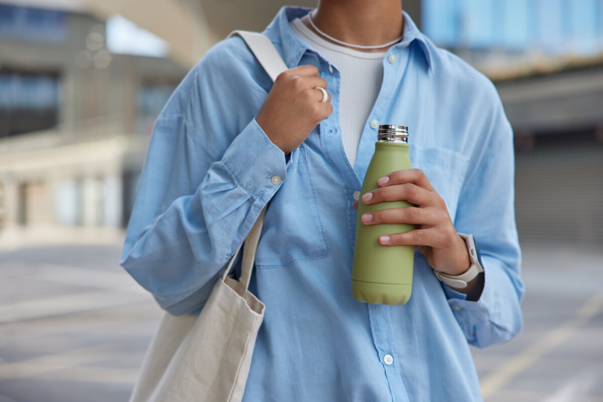 Woman with a tote bag holding an insulated water bottle at a bus stop