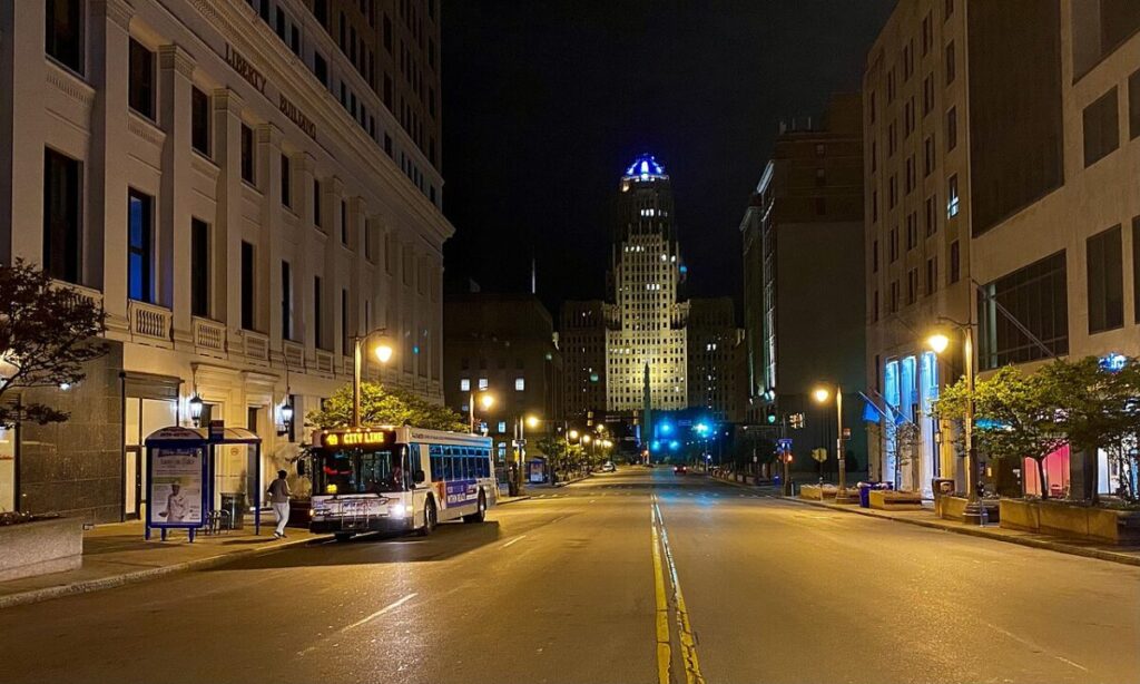 Nighttime urban scene with illuminated buildings, a city bus, and calm street atmosphere.