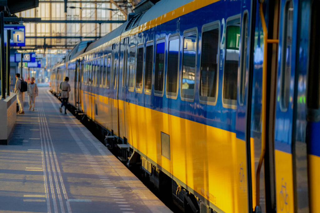 Modern train station scene with vibrant blue and yellow train, passengers boarding and alighting.