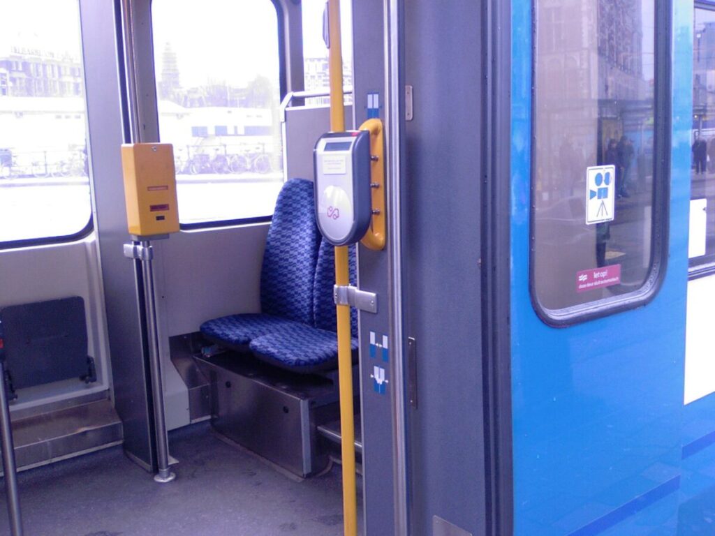 Interior of a clean tram with blue checkered seats and visible ticket validator for passengers.