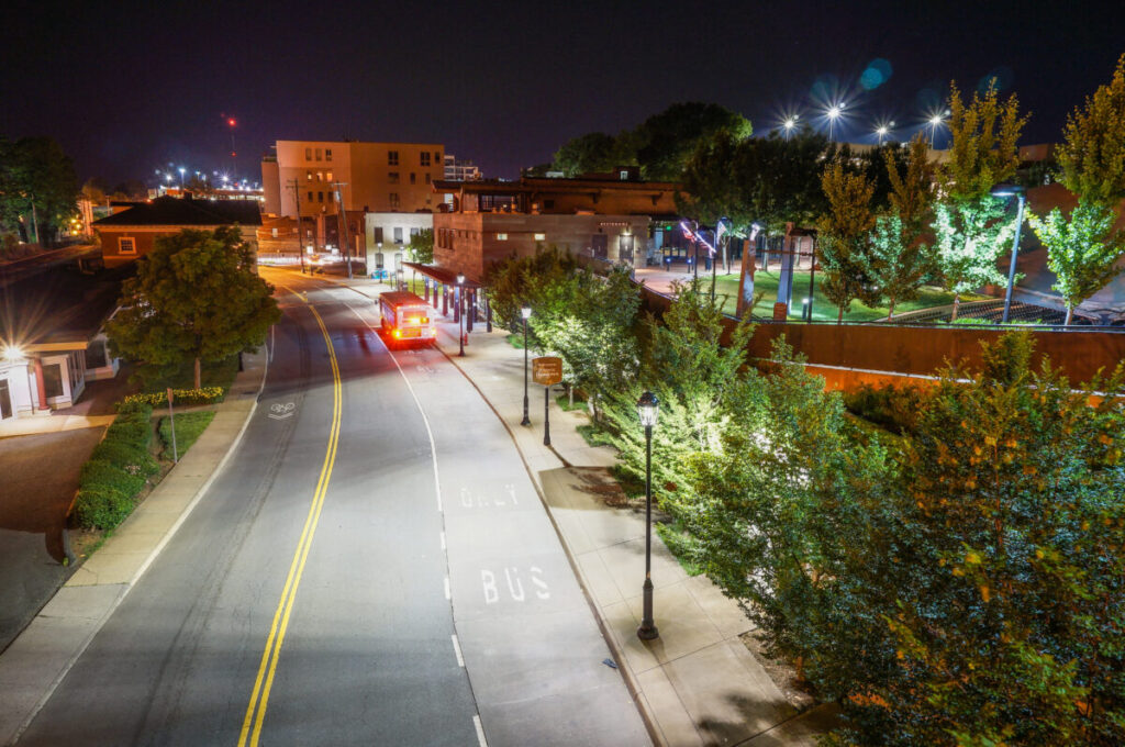 Lively Charlottesville Downtown at night, featuring a bus lane, illuminated buildings, and parks.