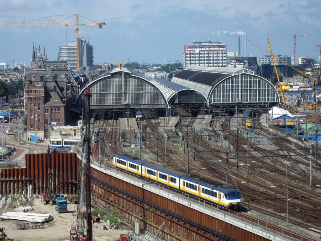Busy urban train station scene highlighting modern architecture and ongoing construction activities.